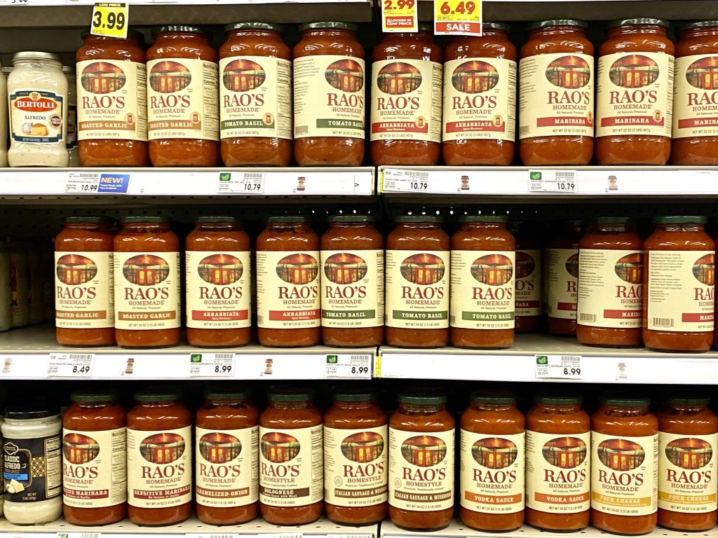 Numerous bottles of Rao's marinara on store shelf.