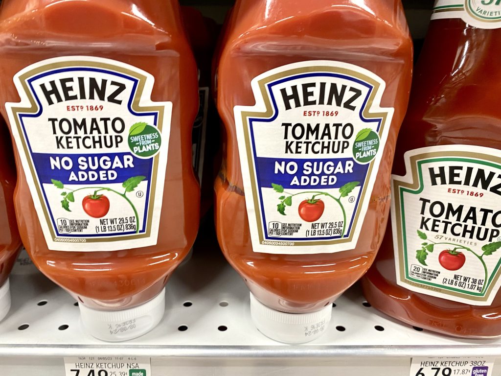 Bottles of reduced sugar ketchup on grocery shelf.