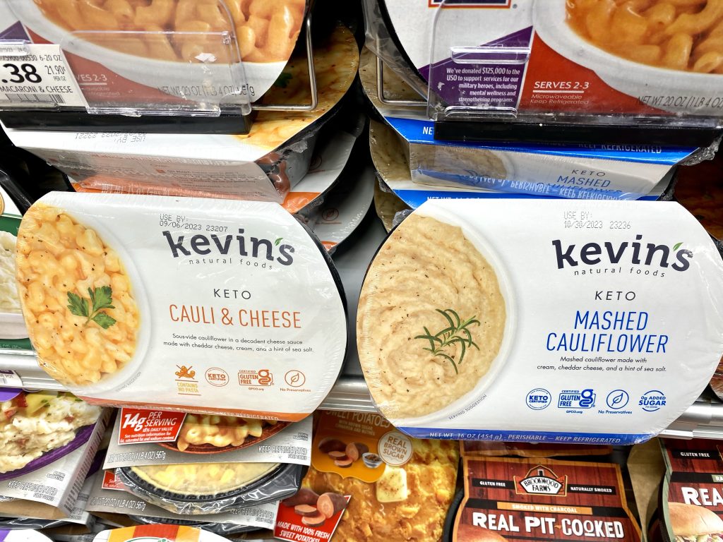 Packages of keto mashed cauliflower and keto macaroni and cheese in the grocery store cooler case.