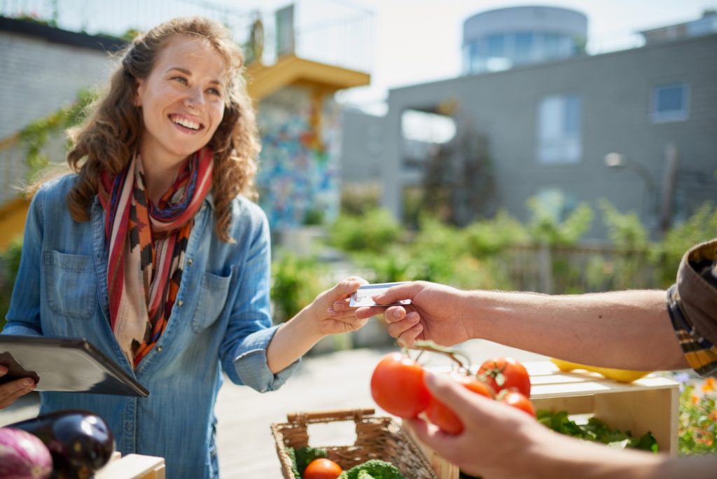 A lady at the farmers market handing someone a card to pay.