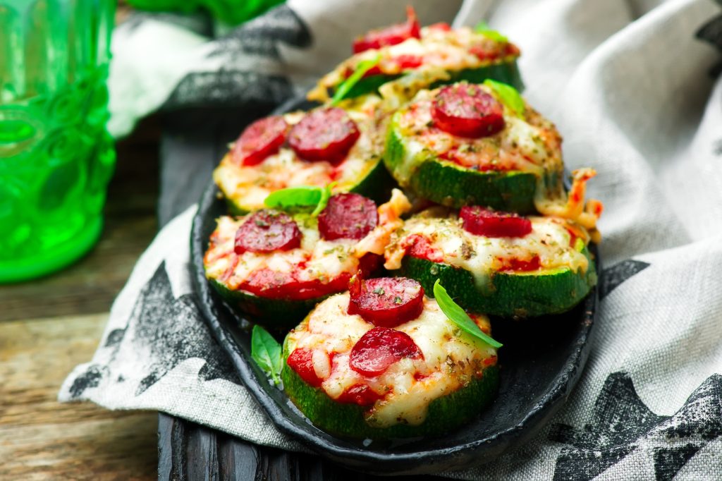 A plate of small pepperoni zucchini slices pizzas.  A black plate and sitting on a hand towel.