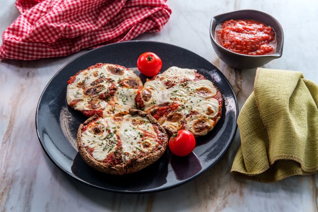 3 pepperoni portabello mushroom pizzas on a black plate. A small bowl of marinara sauce to the side.