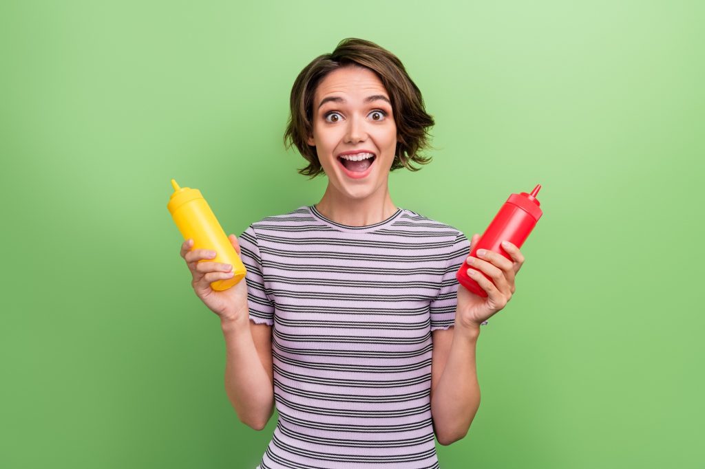 A woman holding a yellow squeeze bottle in one hand and a red one in the other.