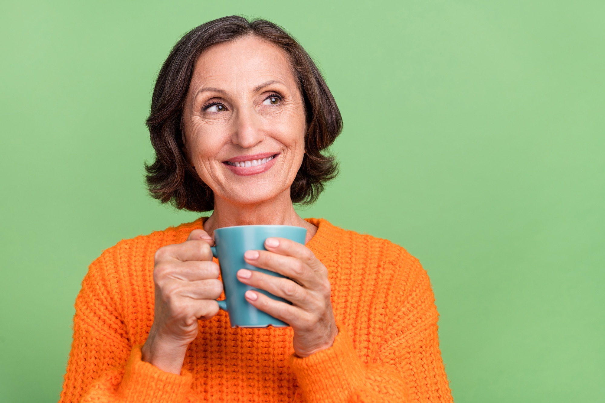 A retired age woman holding a cup of coffee, smiling.