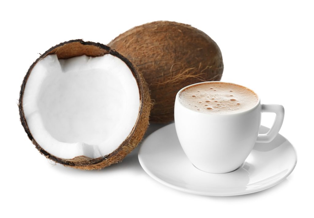 A whole coconut cut in half and a white cup of coffee beside it.