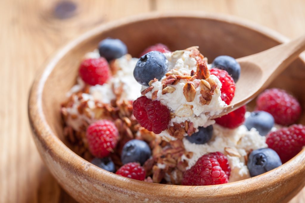 Cottage cheese, berries and granola in wooden bowl.