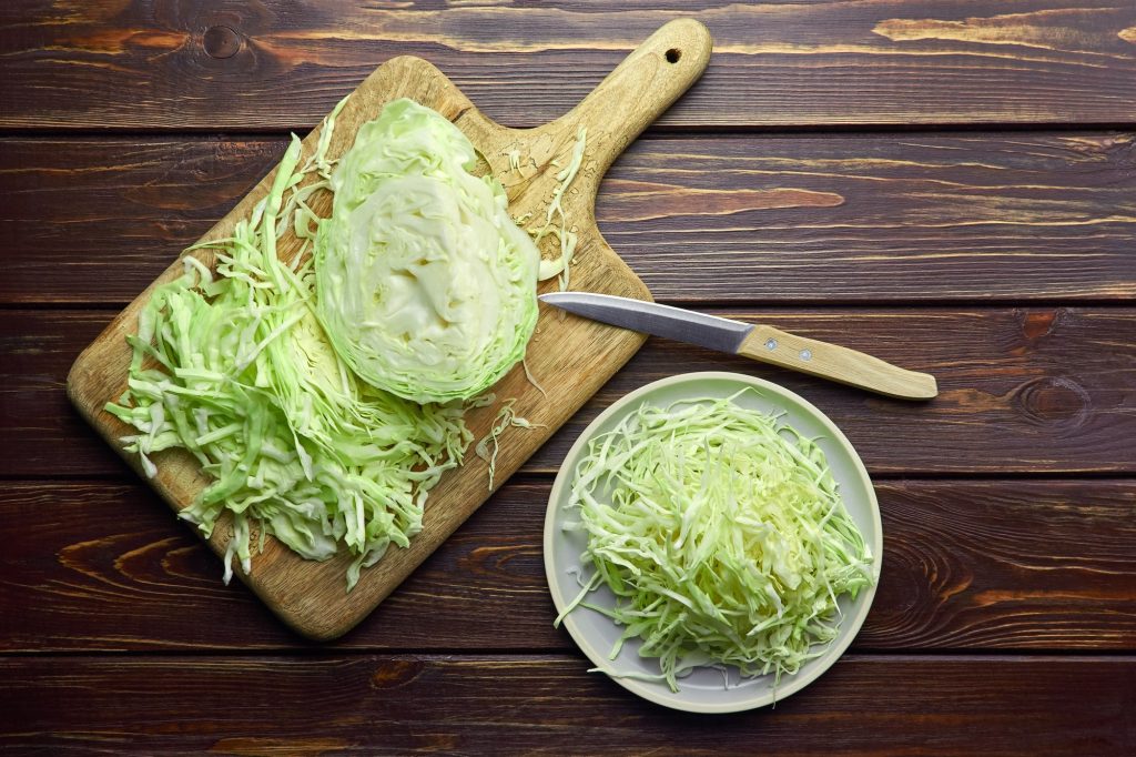 A wood board and knife.  a head of shredded cabbage.