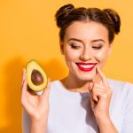 Brunette smiling woman holding half an avocado.