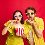 A man and woman eating popcorn, wearing 3d movie glasses.