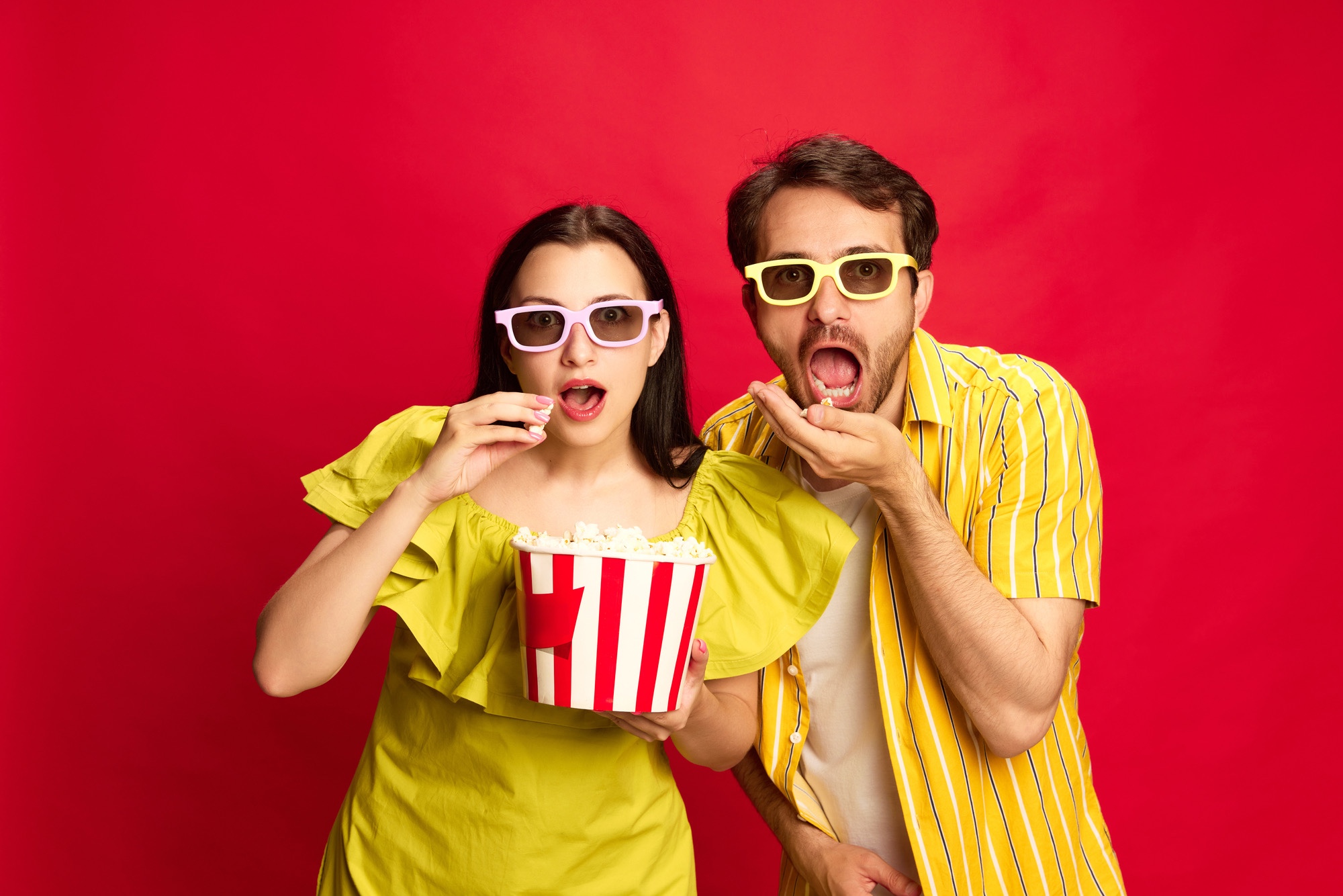 A man and woman eating popcorn, wearing 3d movie glasses.