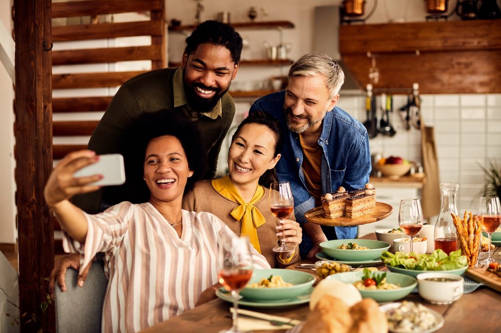 A group of friends, men and women eating together and taking a selfie with a cellphone.