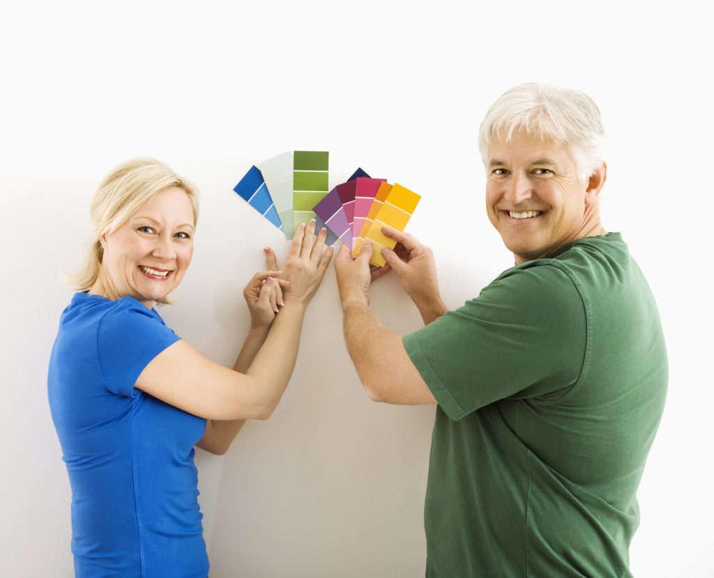 A middle age man and woman holding paint samples up to the wall.  They are both smiling.