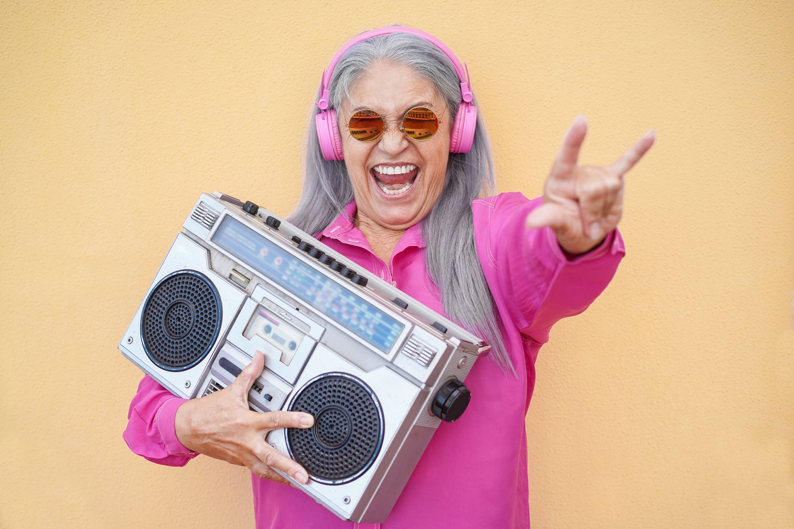 Middle age lady wearing ear phones hold a boombox with mouth open smile.