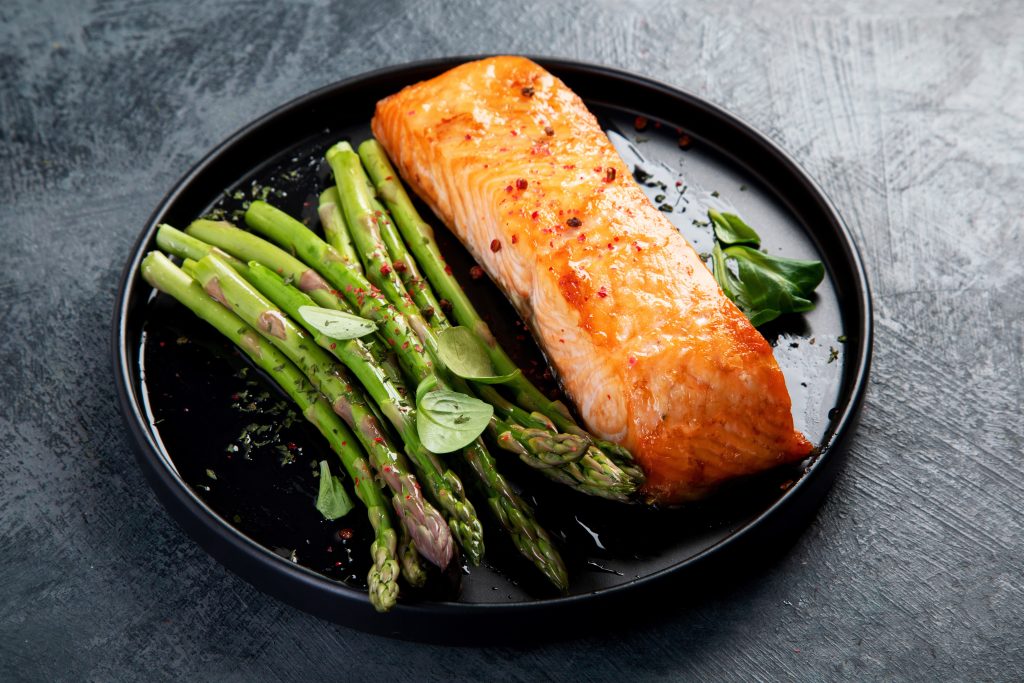 Grilled salmon and asparagus on a black plate.
