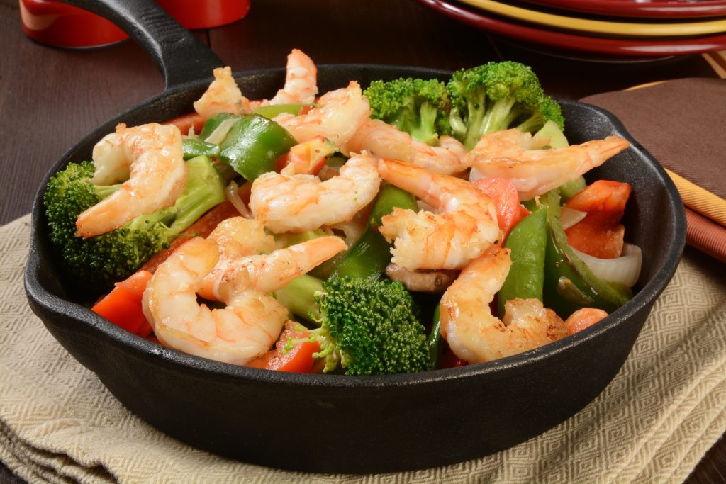 stirfried shrimp and vegetables in a black skillet.
