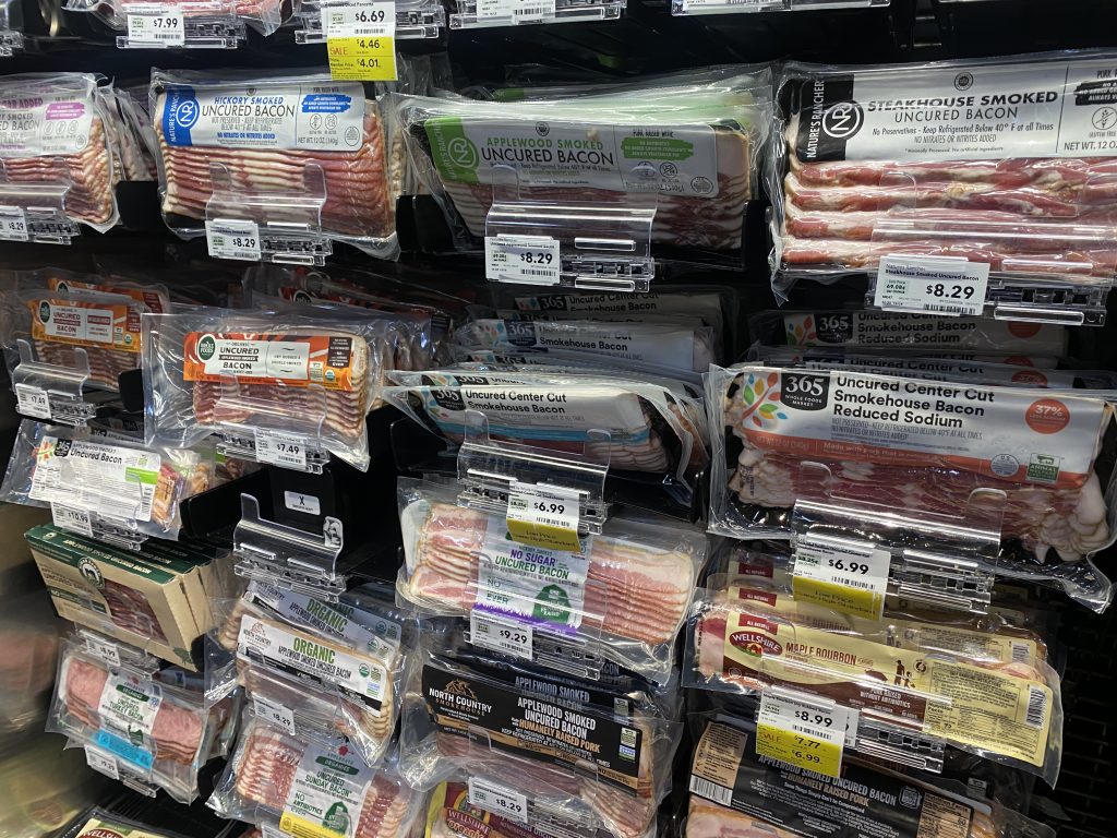 A variety of packages of bacon in the cooler of the grocery.