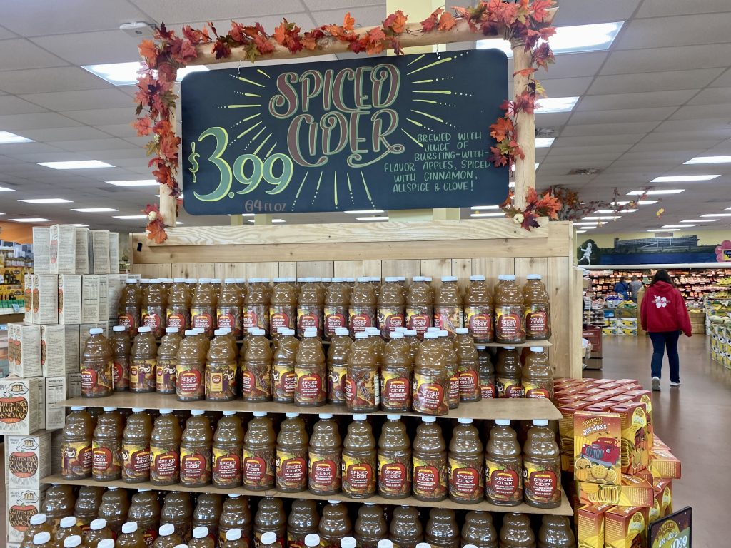 An endcap at the grocery filled with plastic containers of spiced cider.