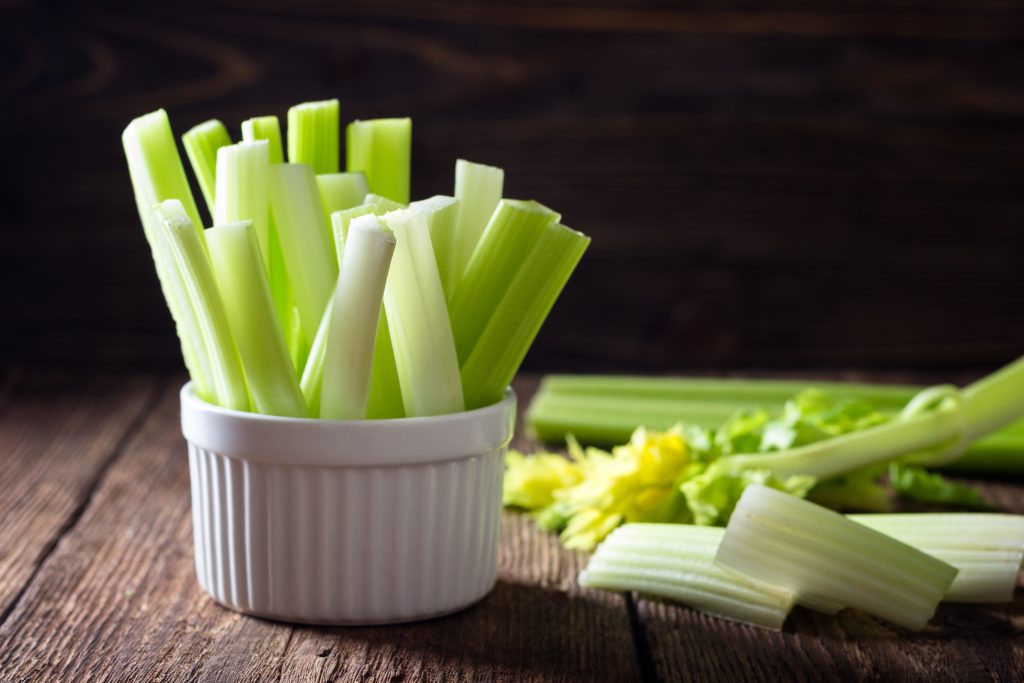 a white bowl filled with celery sticks.  celery beside the bowl as well.