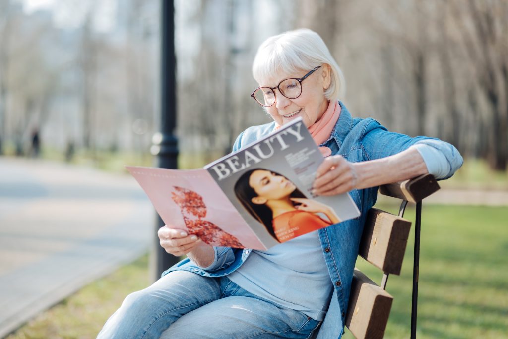 a woman reading a magazine outside on a bench.
