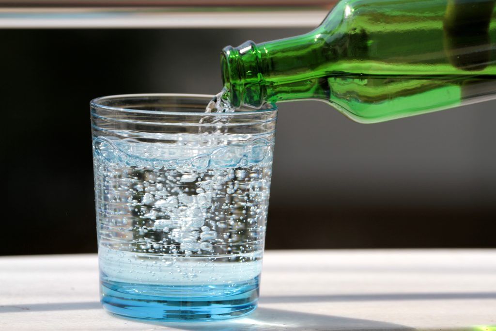 A clear glass and a green bottle pouring mineral water into it.