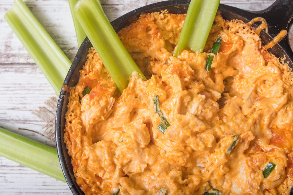 A black skilled filled with buffalo chicken dip, celery sticks are sticking out of it.