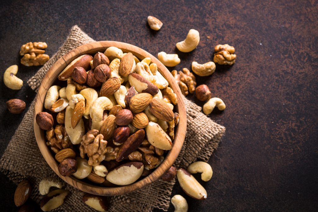 A wood bowl with large variety of mixed nuts in it.