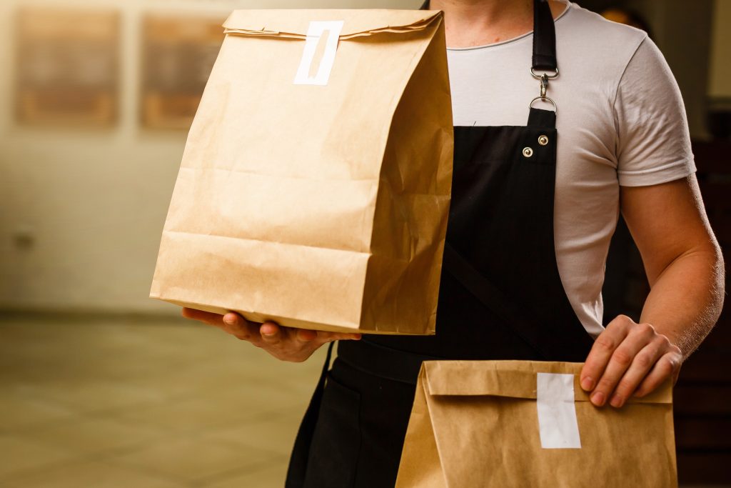 a food delivery person holding two sealed brown paper bags.  