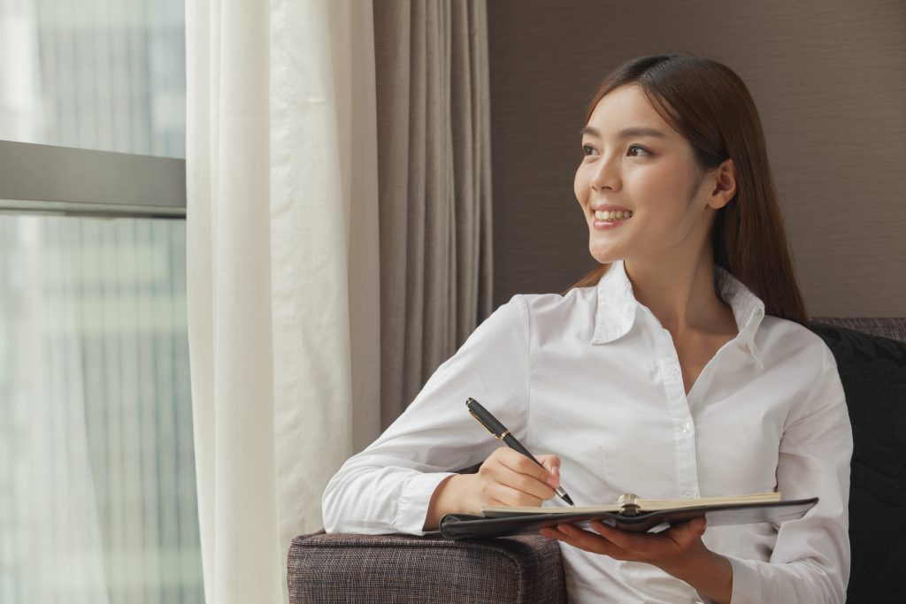 A woman wearing a white button down shirt, writing on a notebook.