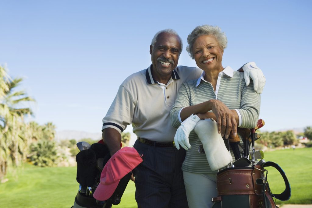 Older man and woman on golf course with their clubs.