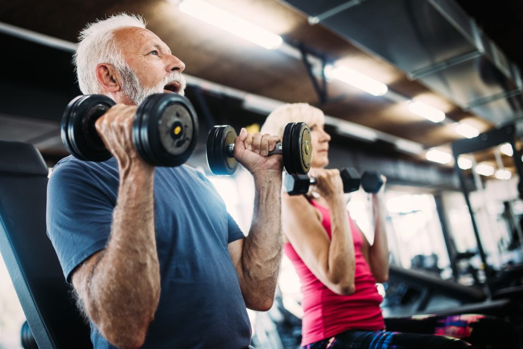 Older man and woman lifting weighs at a gym.