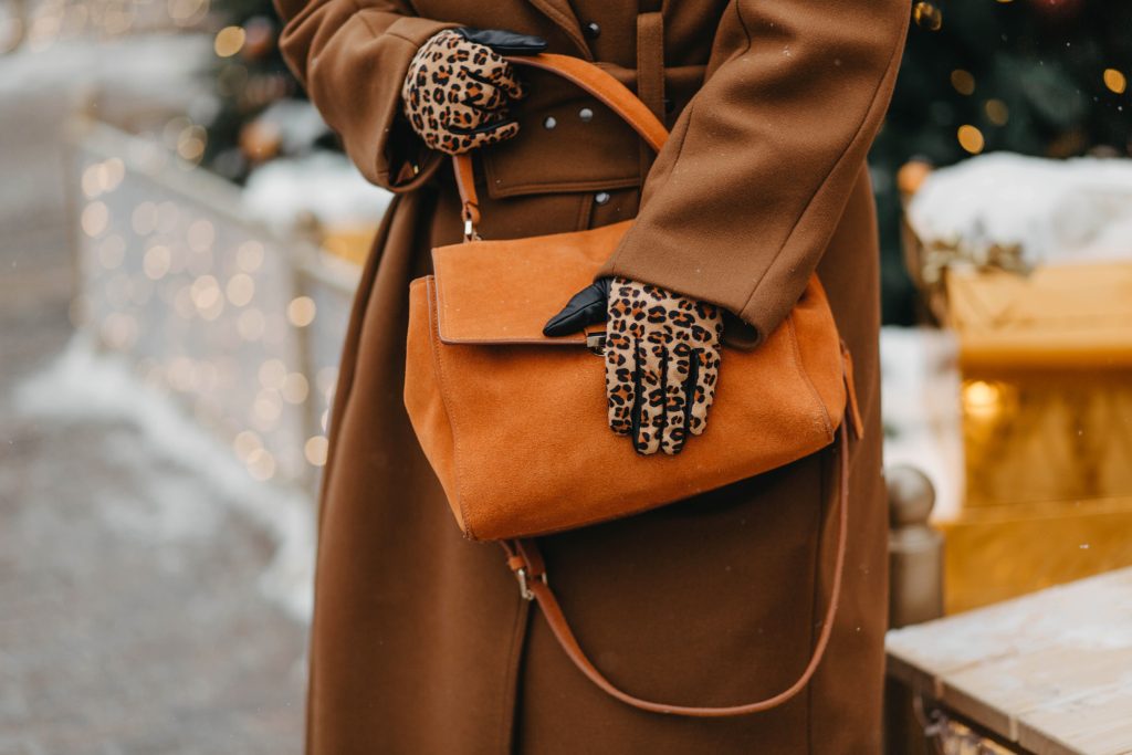 Leopard gloves on a person holding a tan handbag.