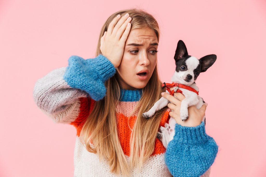 A confused girl with her hand on her head holding a puppy.