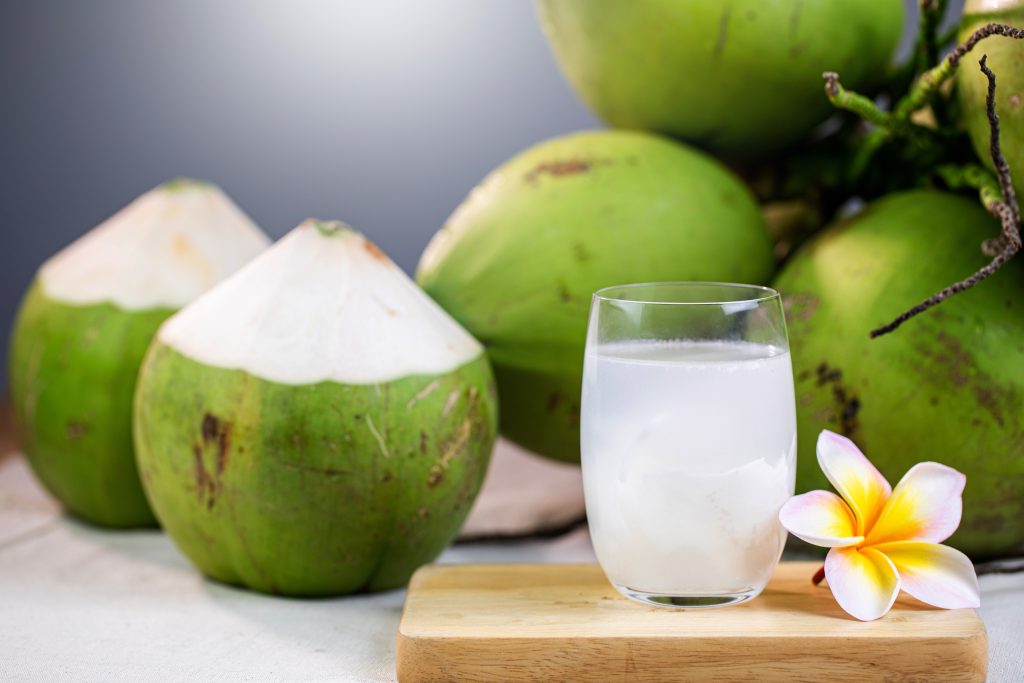 Fresh coconuts and a glass of coconut water sitting on a wood board.  a flower beside the water.