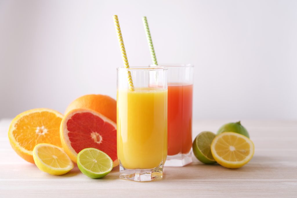 two glasses with two different juices in them. cut fruit laying beside the glasses.