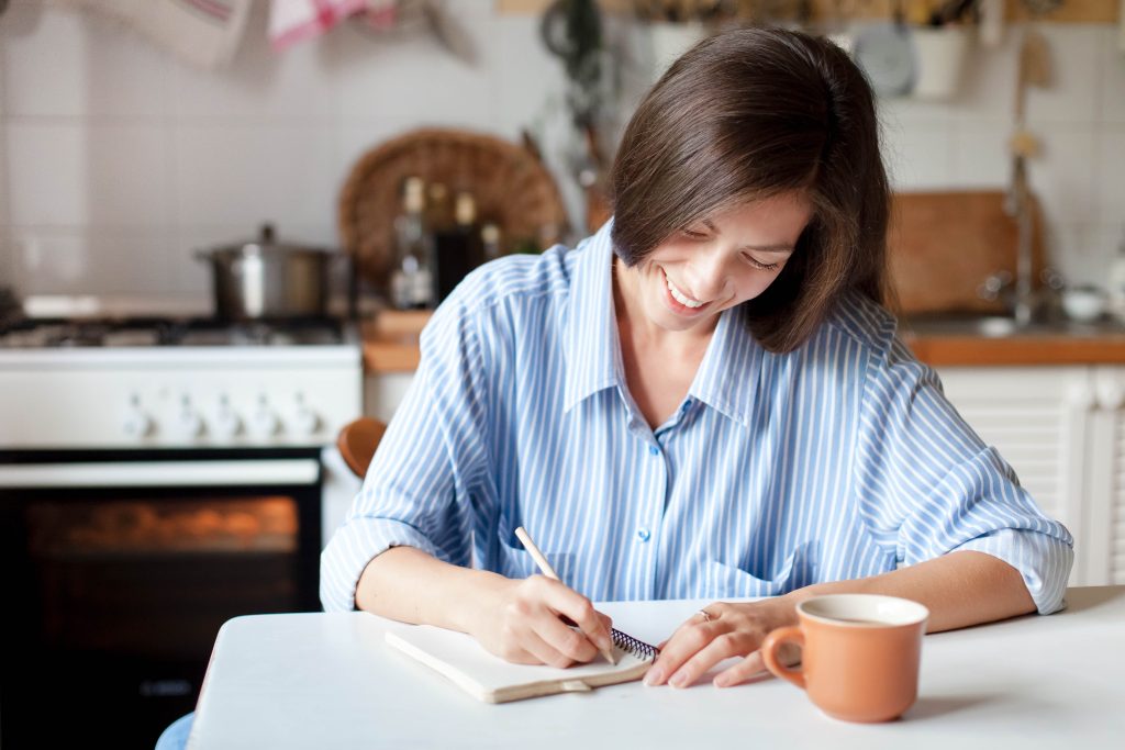 A woman sitting in a kitchen at a table, planning, writing.