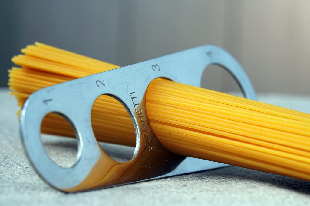 Pasta measurer with uncooked spaghetti sticking out of it.