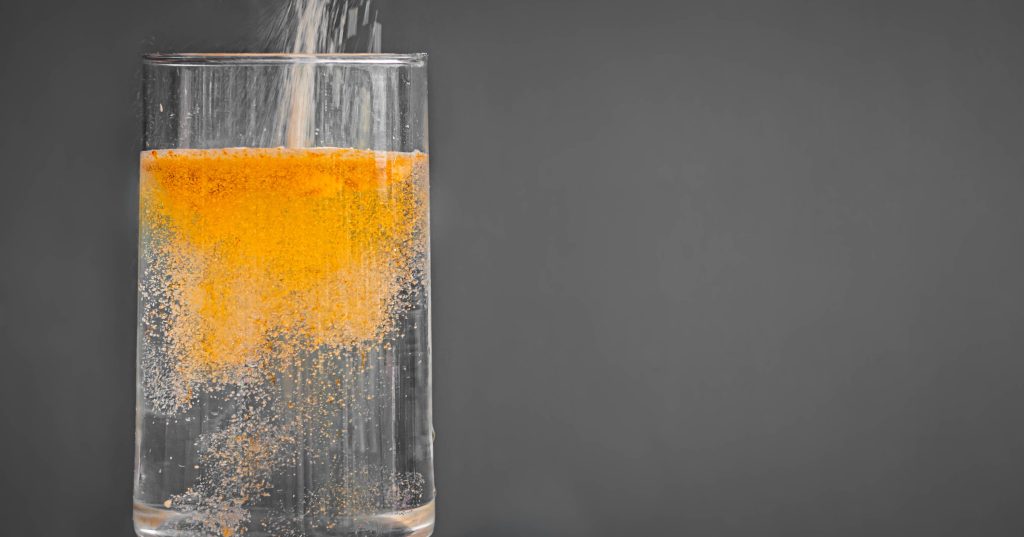 A clear glass of water with orange electrolyte powder pouring into it.