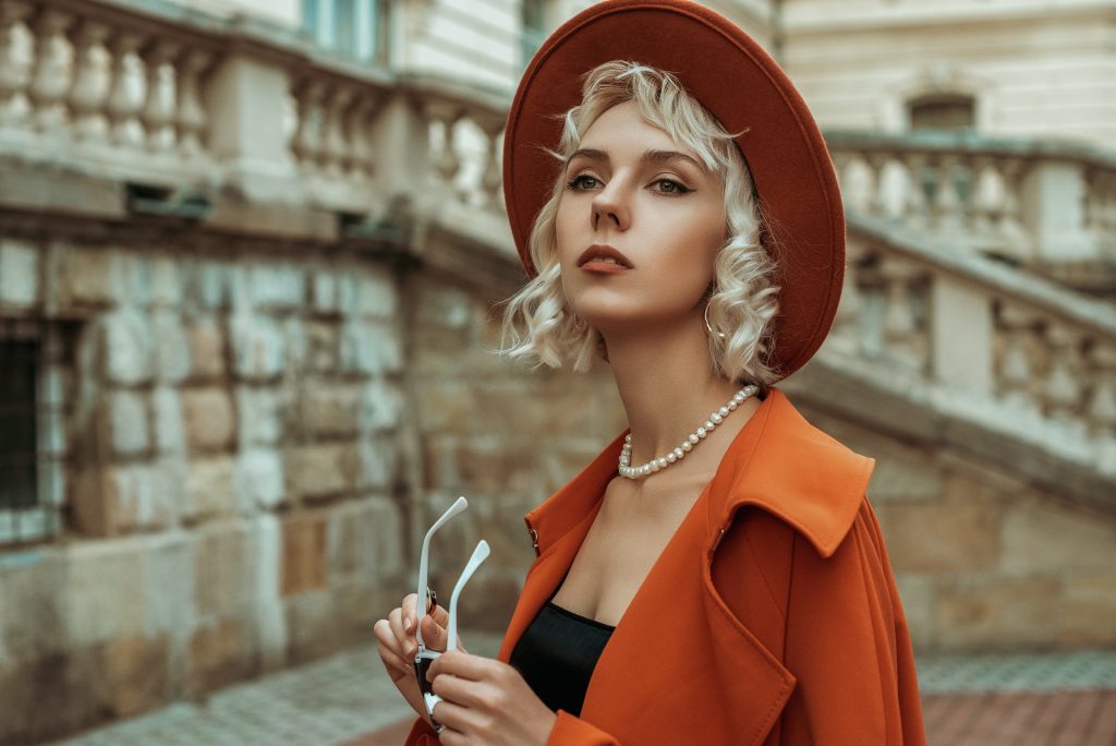 A woman wearing a orange hat and coat accessorized with a pearl necklace.