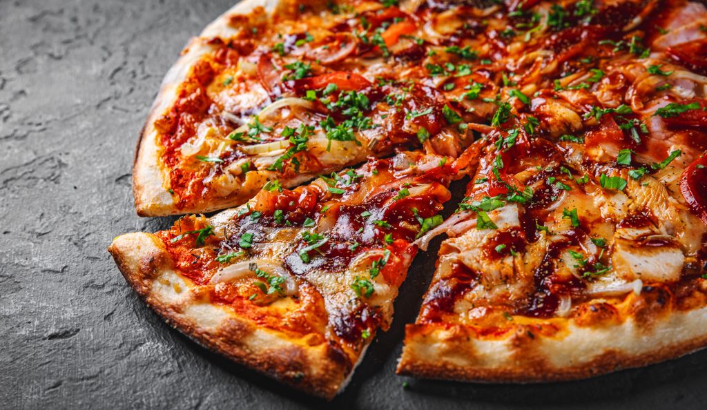 Chicken BBQ pizza sitting on a black background. One piece is cut out of it.