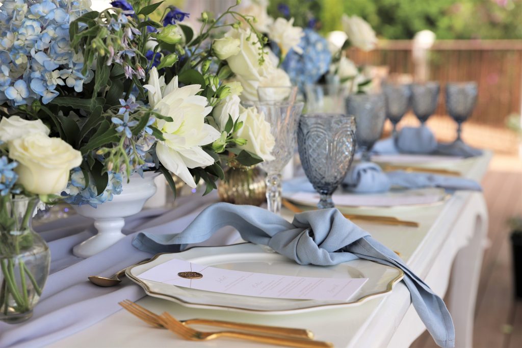 A blue and white elegant table scape.  white dishes, blue napkins, and blue and white floral centerpieces.