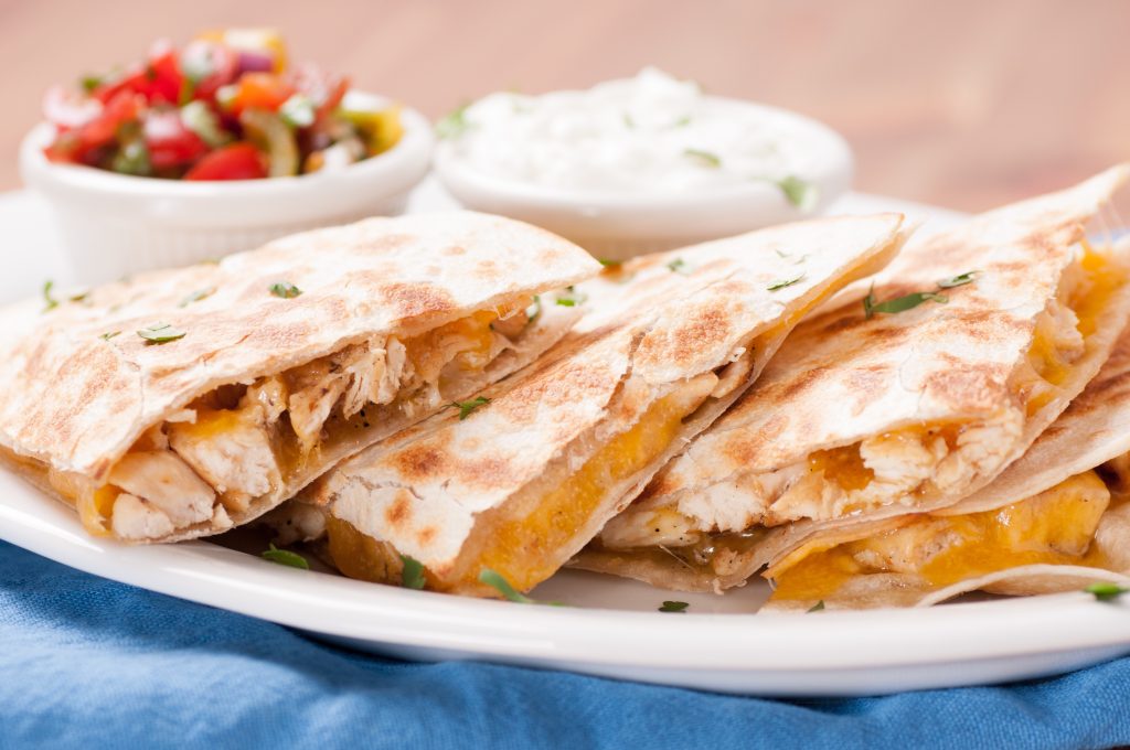 A chicken and cheese quesadilla cut into pieces.  small bowls of sour cream and salsa beside it.