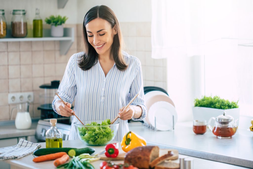 A woman cooking in a kitchen. she's tossing a green salad.