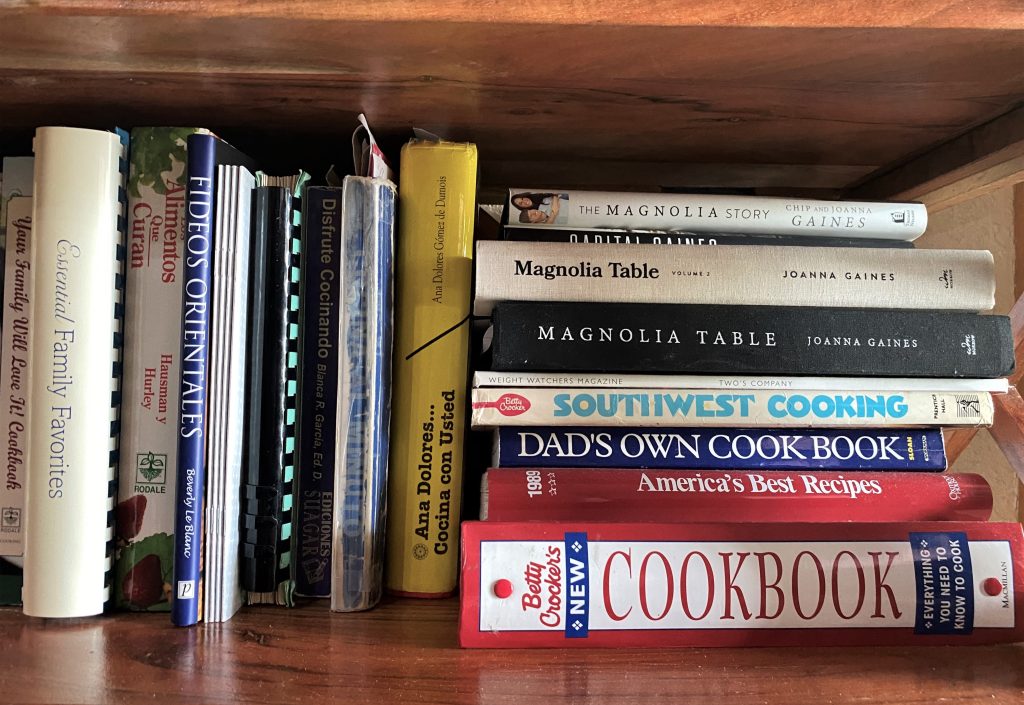 Stacks of cookbooks on a bookshelf.