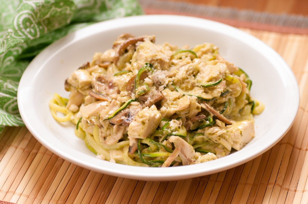 Chicken alfredo and zucchini noodles in a white bowl on a wood table.