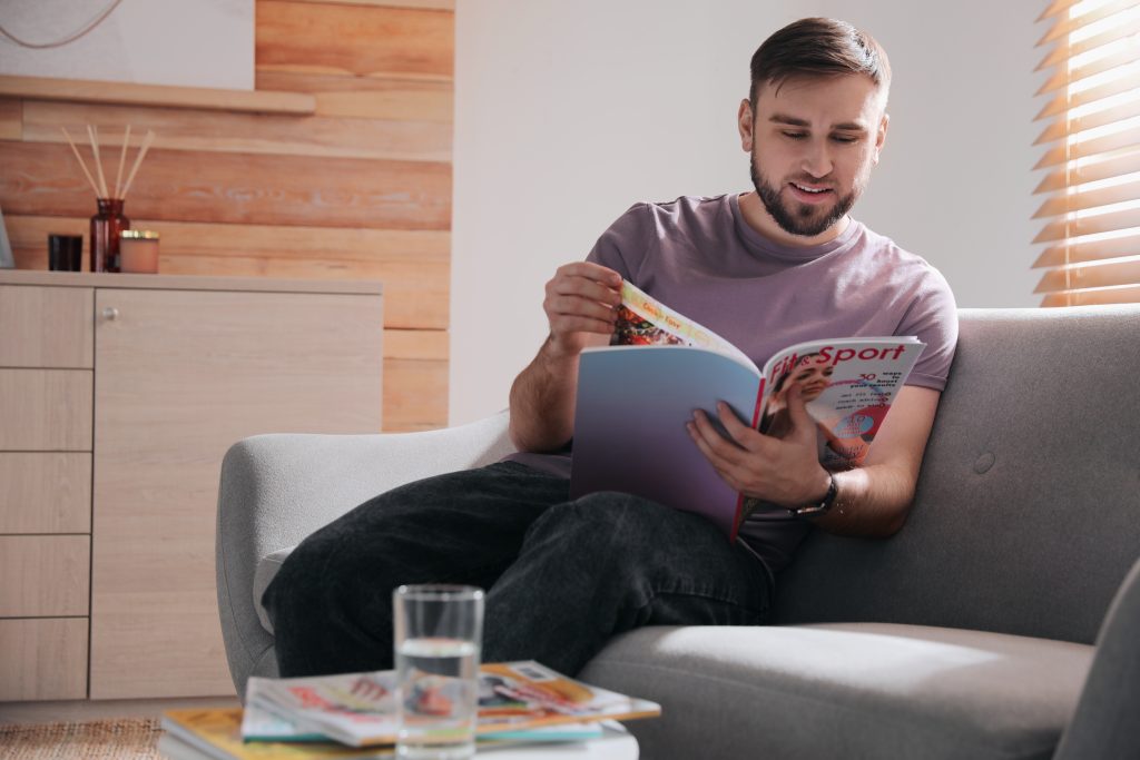 a man sitting on a sofa reading a magazine.