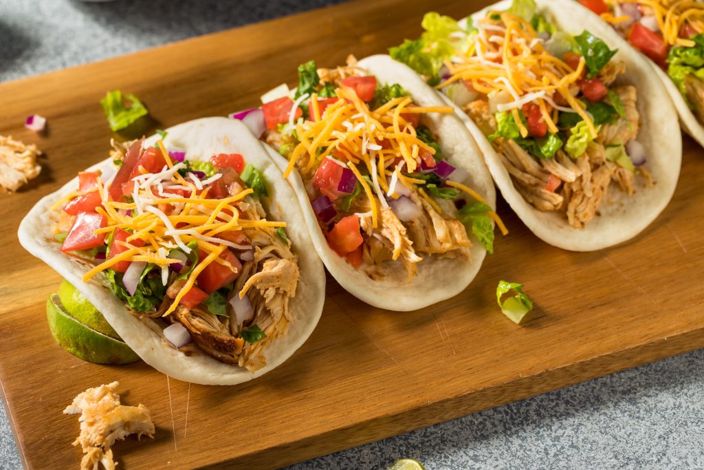 Three chicken tacos with fixings on a wooden board.
