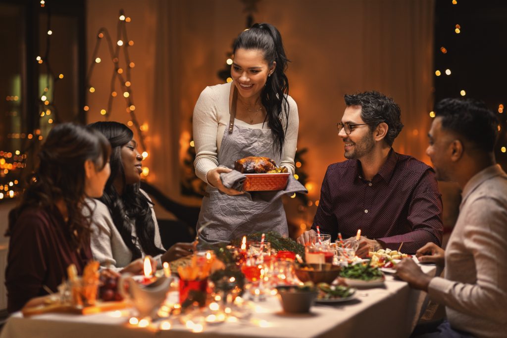 A dinner party with a lot of friends, a female host is standing and serving the table.