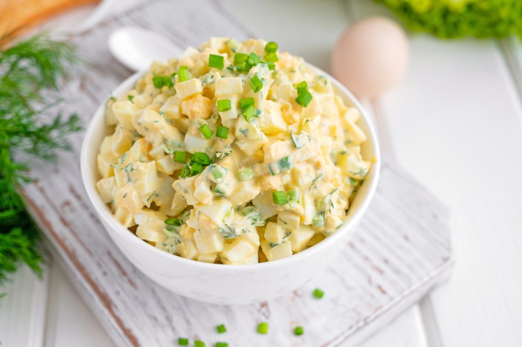 A bowl of egg salad garnished with sliced green onions.