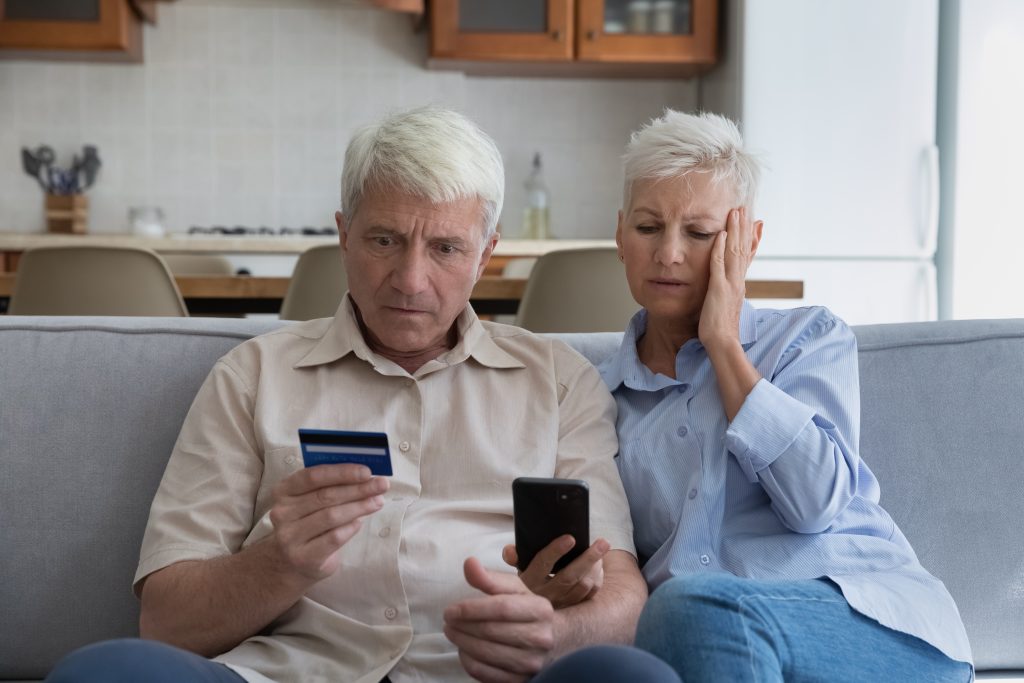 Older couple look confused looking at their credit card and computer.