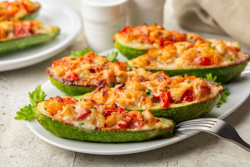 Baked zucchini halves filled with chicken, vegetables and cheese on a white plate.
